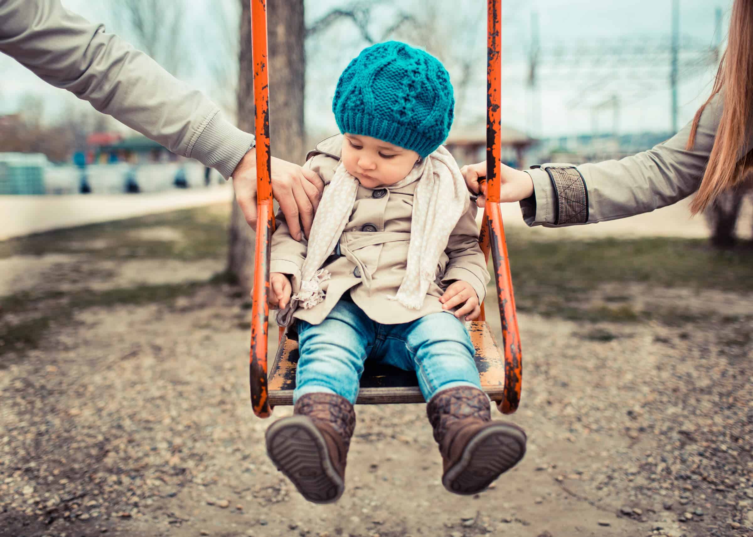 A small girl having fun on a swing, with her parents supporting her on each side.
