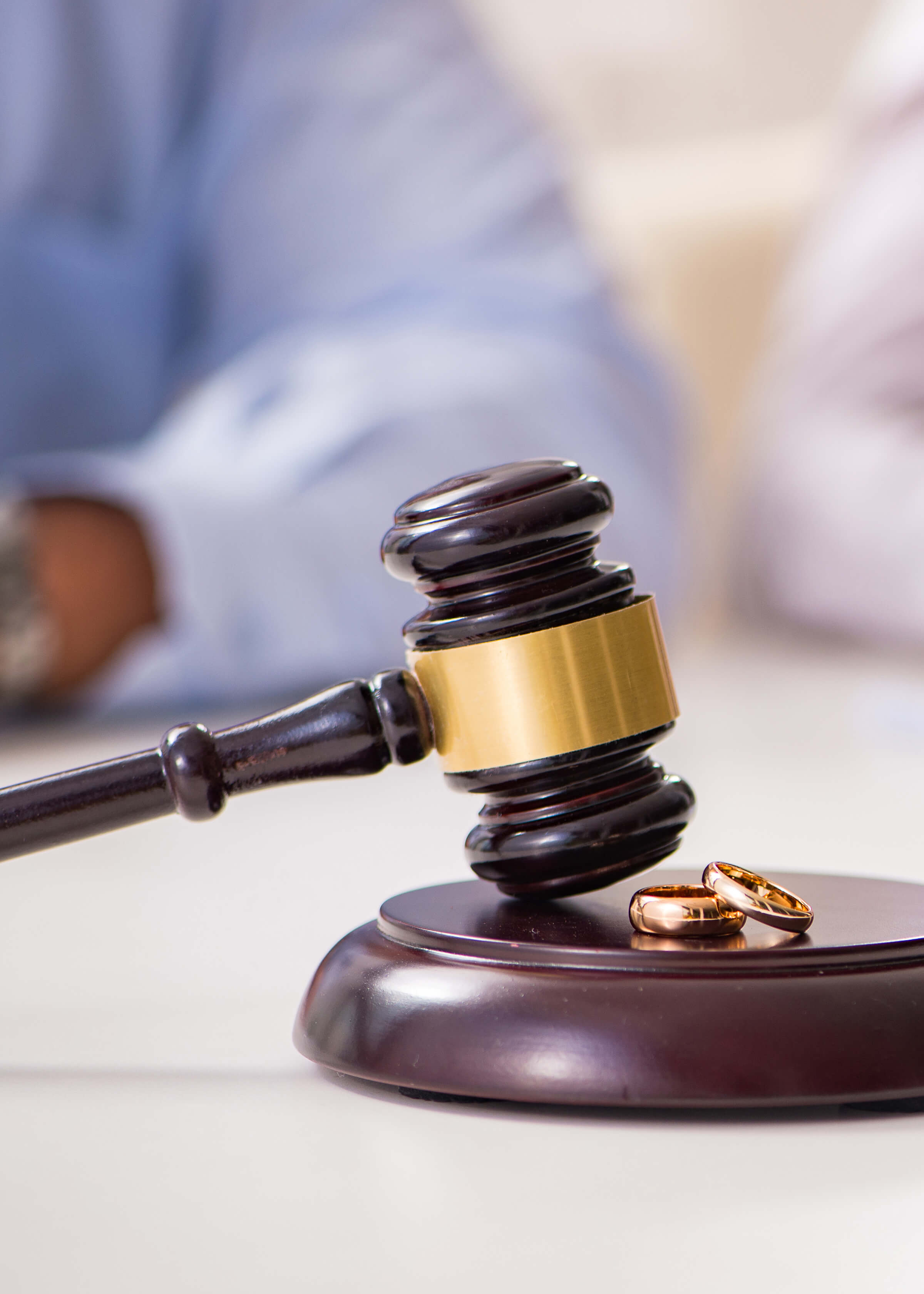 Wedding rings on a judge's gavel, symbolizing divorce, with a divorcing couple signing a document.