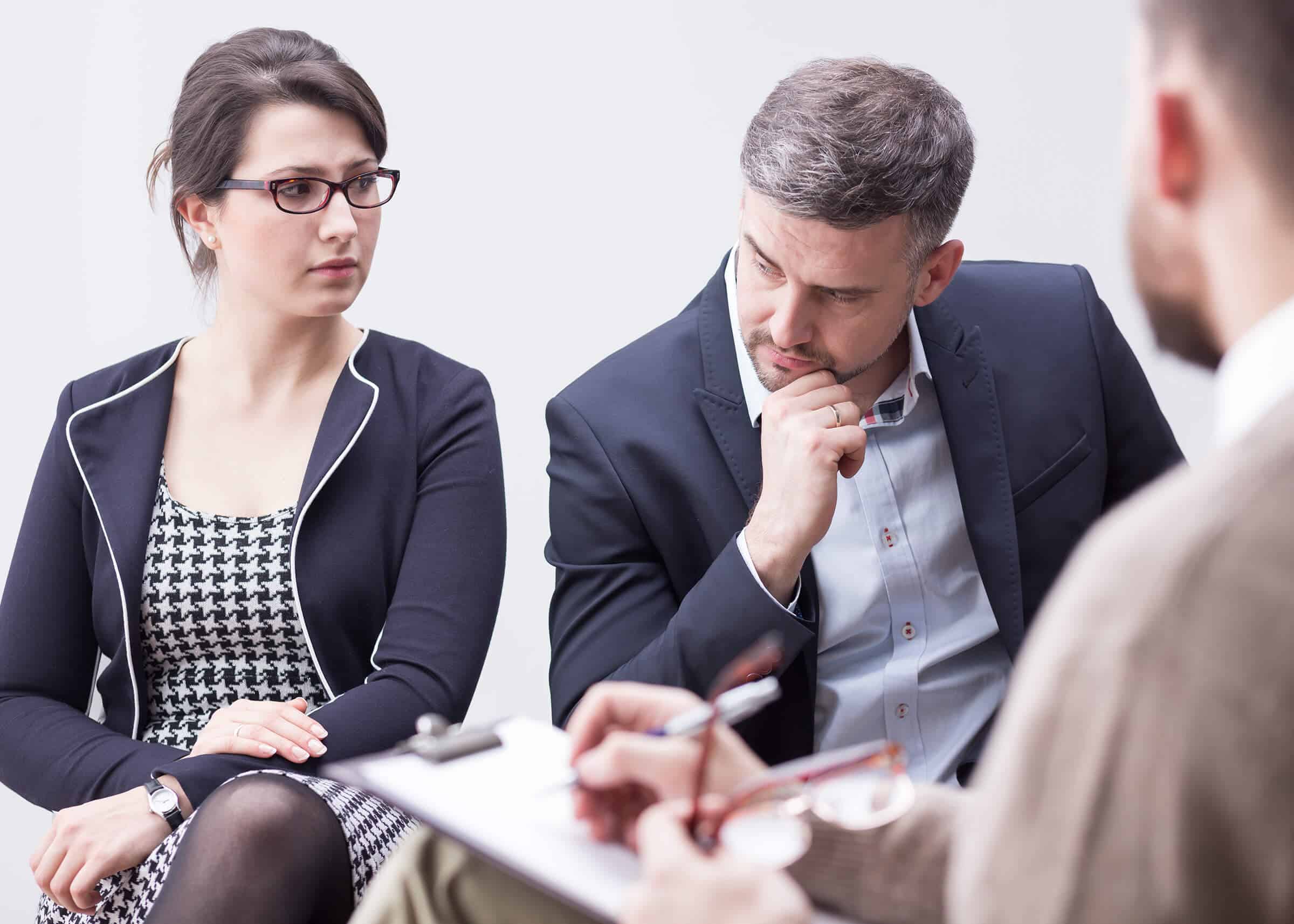 A man and woman in a meeting room with a man in glasses. They are engaged in a divorce mediation session.