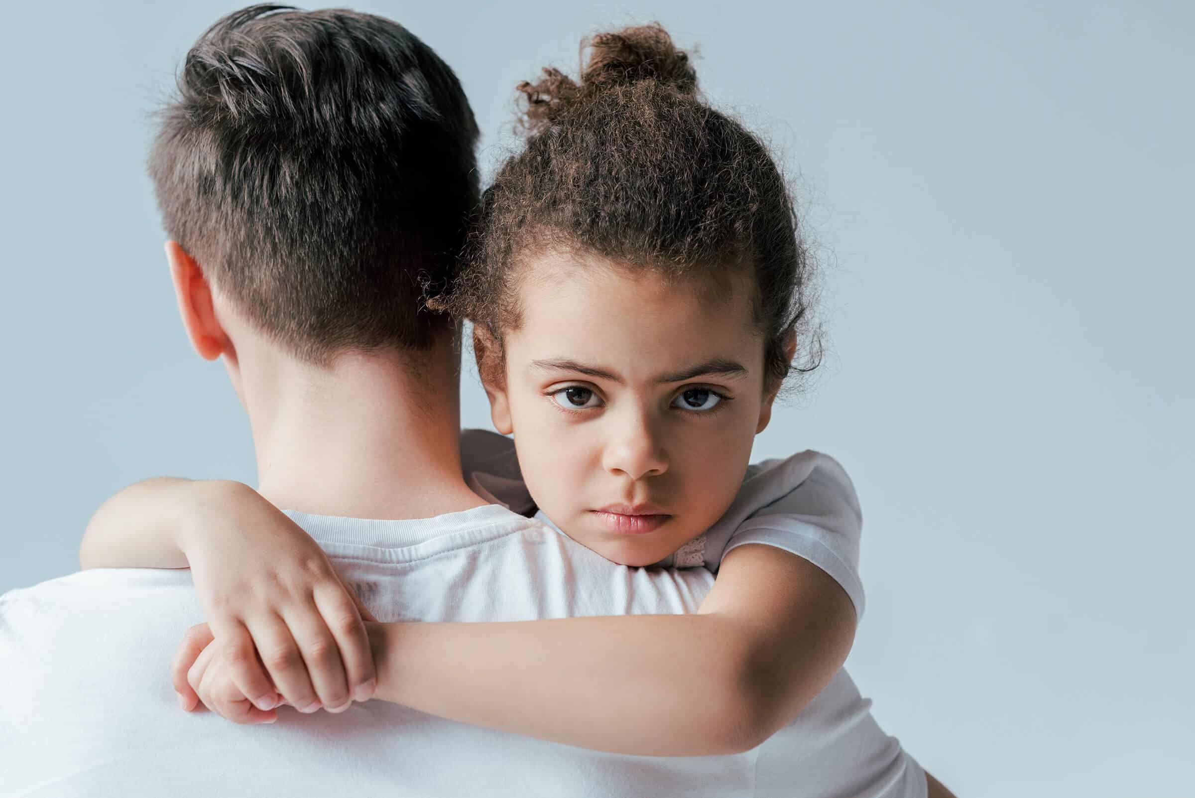 A young girl with a worried expression is tightly embracing her father in a hug.